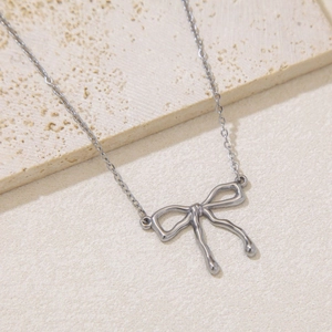 Detail of silver bow pendant with round beads on cross chain against beige stone surface