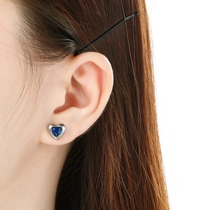 Close-up of blue heart stud earring with silver metal setting worn on model's ear