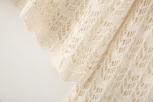 Close-up of intricate crochet hollow-out pattern on beige long sleeve knit top fabric