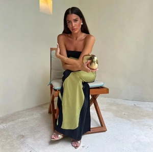 Detail of a black and olive green color-block tube maxi dress worn by a model on a chair