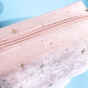 Close-up of pink velvet cosmetic bag with gold star patterns and zipper detail