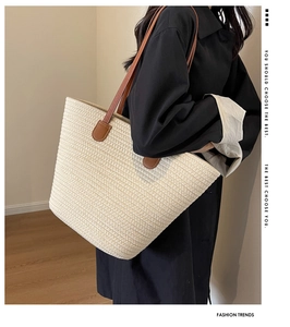 Detail of woven straw tote bag with brown leather handle shown on model in minimal setting