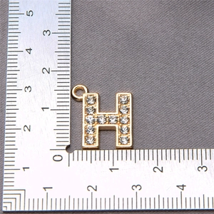 Detailed view of a gold H-letter alloy pendant with rhinestones and scale measurement