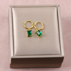 Primer plano de pendientes dorados con cristales verdes rectangulares sobre caja