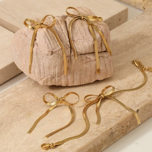 Elegant gold stainless steel bow jewelry set with earrings and tassel bracelet on stone