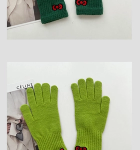 Detailed close-up of green knitted gloves featuring red bow embroidery and ribbed cuffs