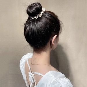 Detail of a beige satin scrunchie showing elegant silk pleats on a bun hairstyle