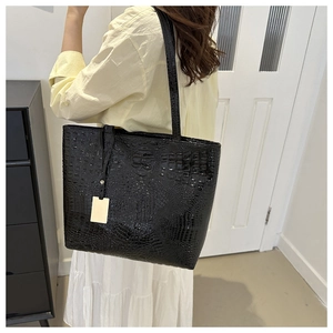 Detail of black crocodile texture tote bag with gold charm worn by model
