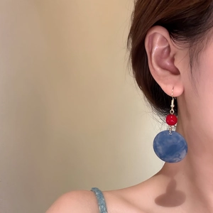 Geometric acrylic drop earrings with red bead and blue marbled pendant on model