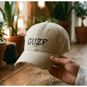 Close-up of black GUZF letter embroidery on distressed beige cotton baseball cap