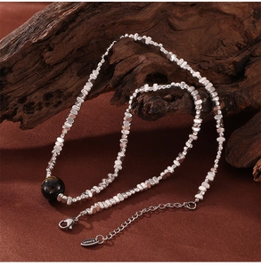 Macro detail of stainless steel beaded necklace with black bead on brown silk fabric