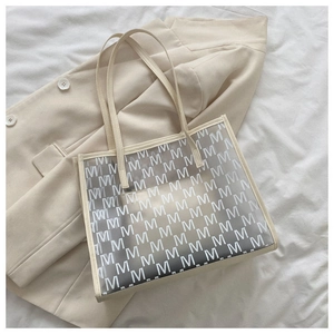 Detail of transparent gray tote bag with M-pattern print on beige blazer background