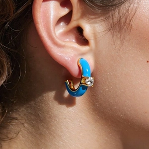Detail view of sky blue enamel C-shape earring with gold base and white zircon on model