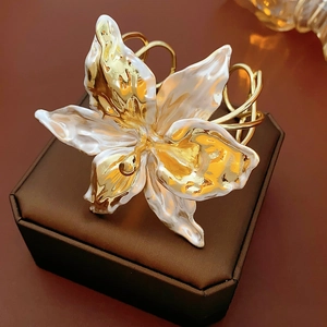 Detailed close-up of a hollow lily flower cuff bracelet in gold and pearl white enamel