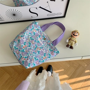 Dettaglio della borsa da pranzo in tela floreale con manici viola intrecciati e bottone