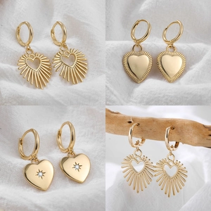 Macro detail of four pairs of 18K gold heart-shaped earrings with rhinestones on white fabric