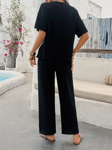 Rear view of black short sleeve top and wide leg pants set in a resort pool setting