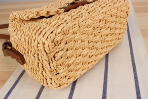 Detailed close-up of beige woven texture with brown leather strap on a straw crossbody bag