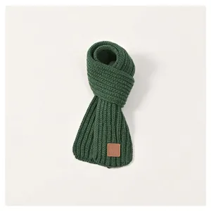 Detail of dark green knit kids scarf with thick vertical stripes and brown leather label