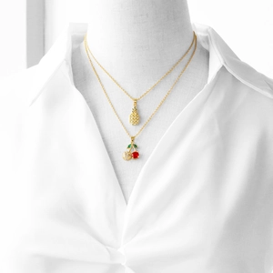 Detail showing elegant gold pineapple and red cherry crystal pendant necklaces on a model