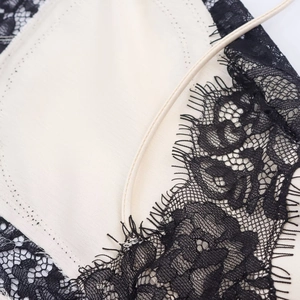 Détail de la broderie en dentelle noire sur la robe sans manches de couleur blanc cassé