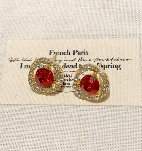 Detalle de pendientes vintage con cristal rojo y halo en acabado dorado.