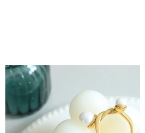 Detailed shot of golden twisted wire bangle with two pearls on a white textured dish