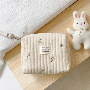 Quilted cotton diaper bag with olive embroidery shown on a warm aesthetic background