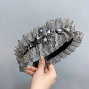 Close-up of luxury grey pleated headband with sparkling large rhinestones held in hand