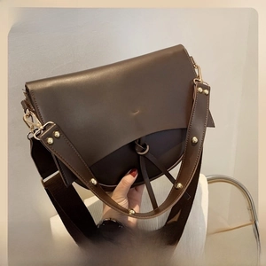 Detail of vintage wide shoulder strap with gold rivets on dark brown saddle bag