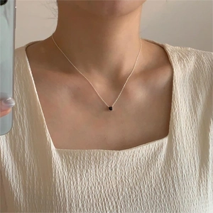 Close-up of minimalist silver necklace with square black zircon pendant on a model