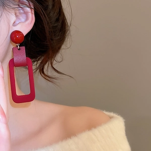 Close-up of red geometric earrings with leather texture and glossy resin beads
