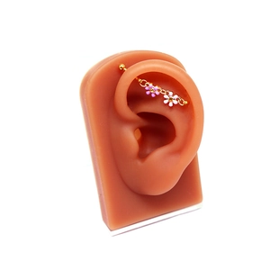 Vue macro d'un piercing industriel doré avec des fleurs roses et des chaînes sur l'oreille