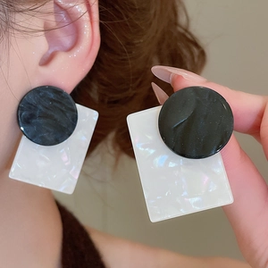 Close-up of geometric black and white square shell drop earrings worn on the ear