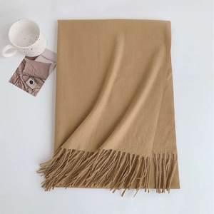 Detailed view of camel cashmere scarf texture and fringe on a minimalist white surface