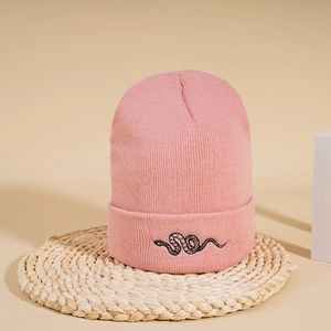 Close-up of pink ribbed knit beanie with black snake embroidery on a woven mat