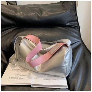 Detail der silbernen Metallic-Handtasche mit pinkem Gurt auf einem offenen Buch