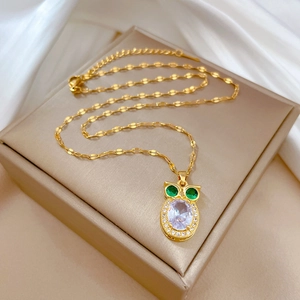Detailed close-up of golden owl necklace featuring green gem eyes and clear crystals
