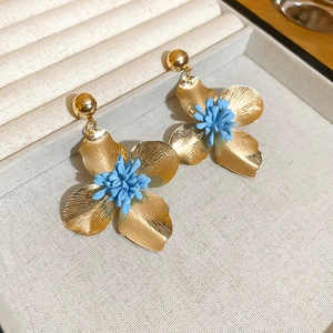 Detailed shot of golden metal flower earrings featuring vibrant blue floral stamens