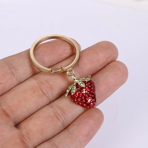 Close-up of a textured red strawberry keychain with green leaves held in hand