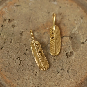 Macro shot of two vintage golden feather pendants on a warm stone surface