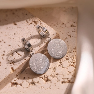 Silver stainless steel Evil Eye round hoop earrings displayed on a beige stone