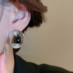 Nahaufnahme eines silbernen gedrehten Ohrrings mit einer schwarzen Perle auf dem Ohr