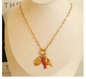 Detail of gold paperclip chain necklace with heart, chili, and hand gesture charms