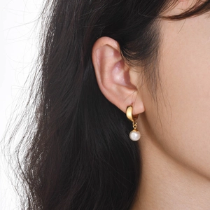 Close-up of golden hoop earrings with white pearl pendants on female model ear