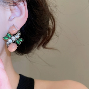 Close-up of vintage earrings with pink cat-eye stone, green gems, and pavé crystals