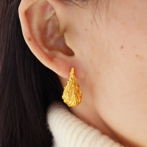 Minimalist gold teardrop earrings with textured flame design on female model