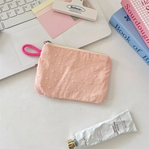 Pink polka dot fabric coin purse with zipper closure and hand strap on a desk
