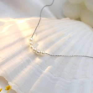 Minimalist 18k silver steel necklace with six white pearls displayed on a white shell