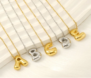 Detailed macro view of 18K gold and silver bubble letter pendants A-E on a textured tray